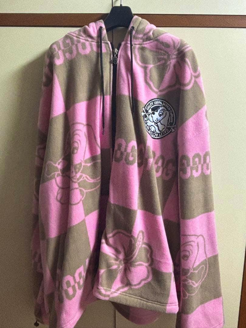 Front view of a pink and brown checkered hooded zip-up top with a dog logo patch hanging on a hanger.