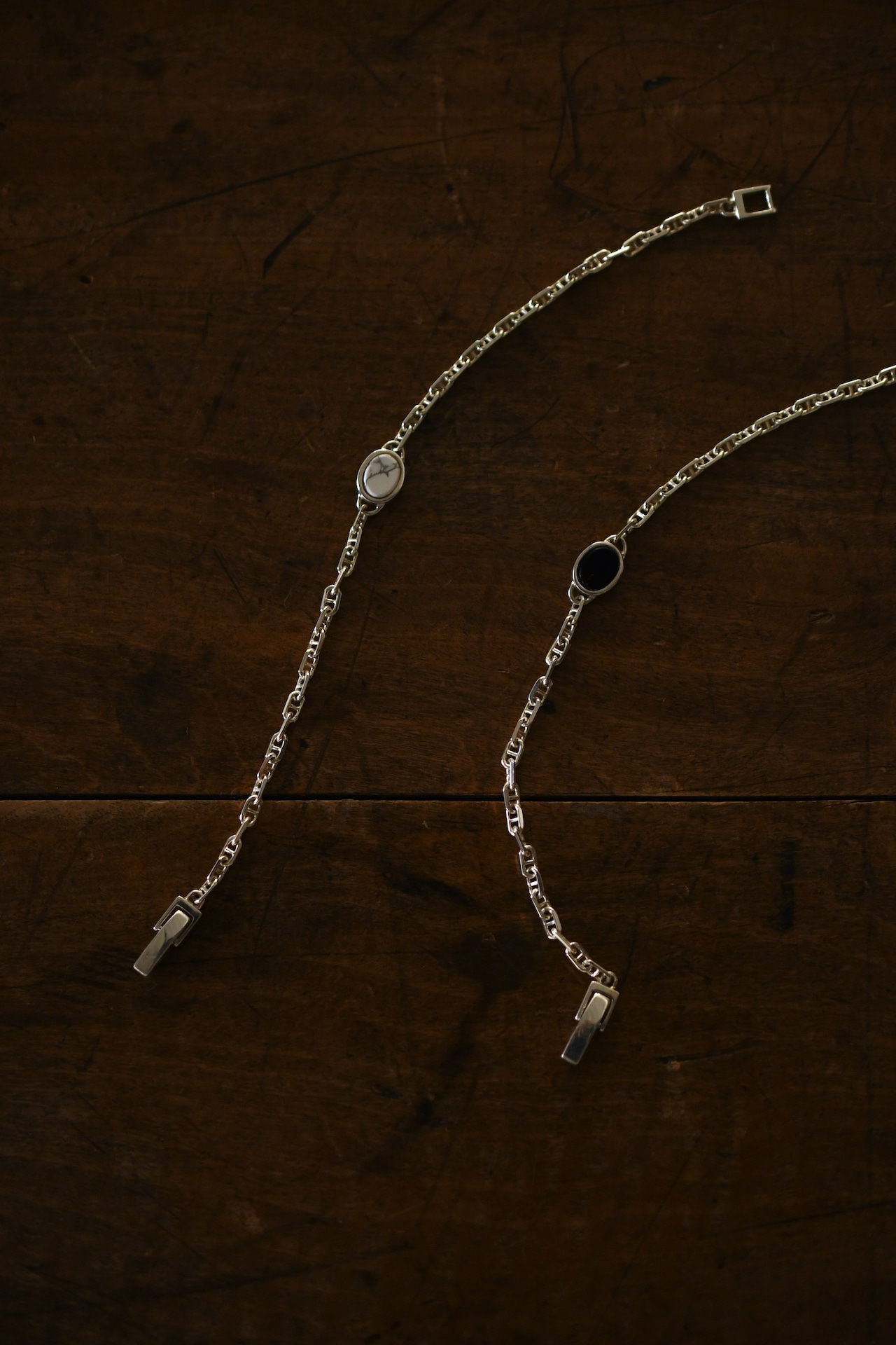 Two silver stone anchor-chain bracelets (onyx and howlite) laid on a dark wooden surface.