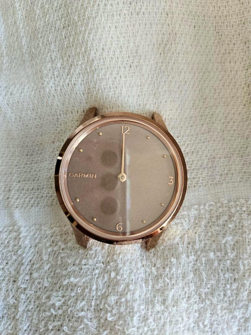 Rose gold Garmin Vivomove Luxe watch body front showing an analog dial without a strap on a textured fabric background.