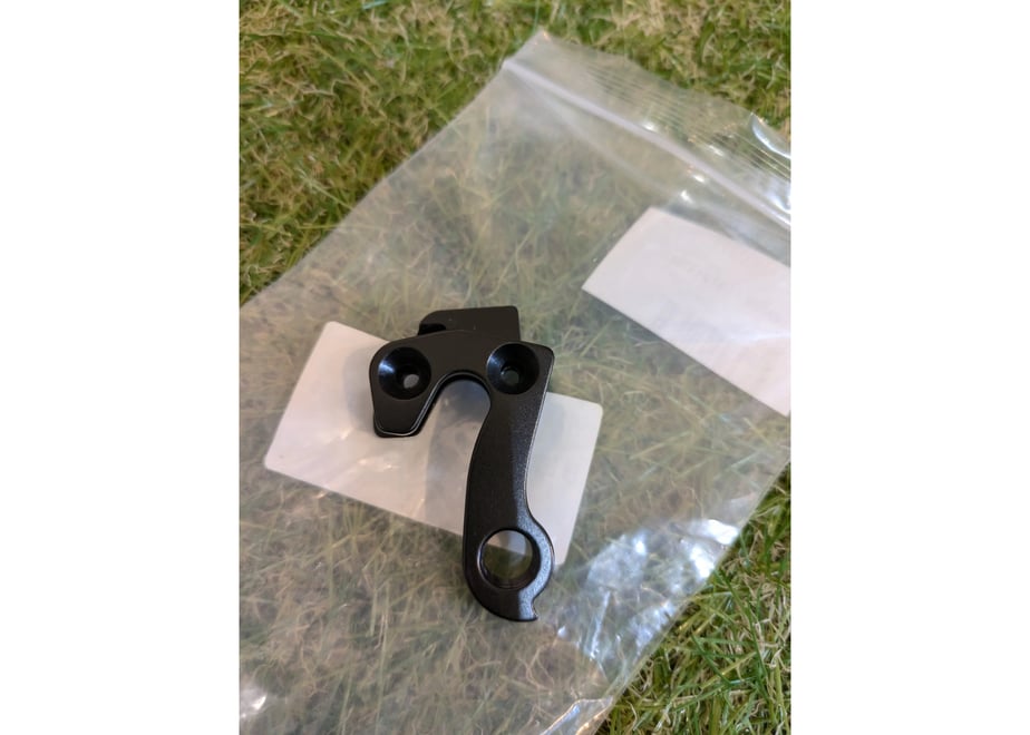Black bicycle derailleur hanger placed on a clear plastic bag on grass.