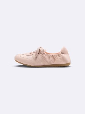 Side view of a gathered ballet sneaker on a plain background.