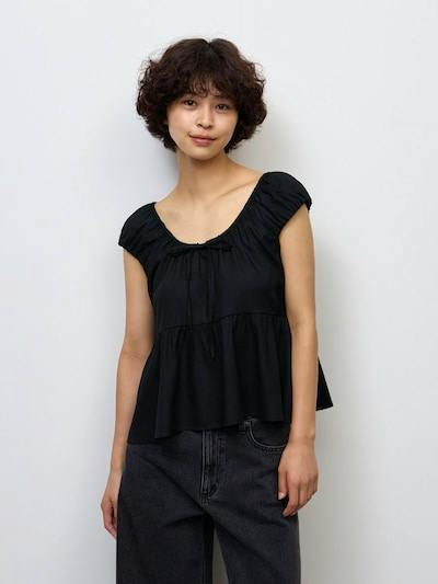 Woman wearing a black sleeveless gathered peplum blouse shown from the front.