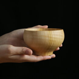 A wooden soup bowl held in two hands against a black background.