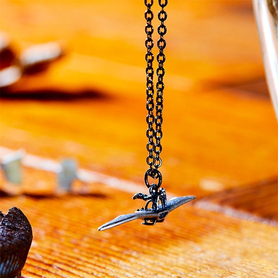 Close-up of the メーヴェ pendant necklace hanging from its chain against a wooden surface.
