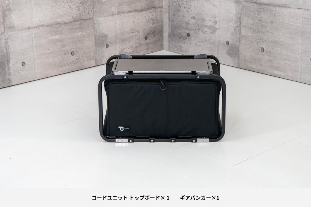 Black gear basket with a tubular metal frame and fabric body placed on a studio floor with concrete walls.