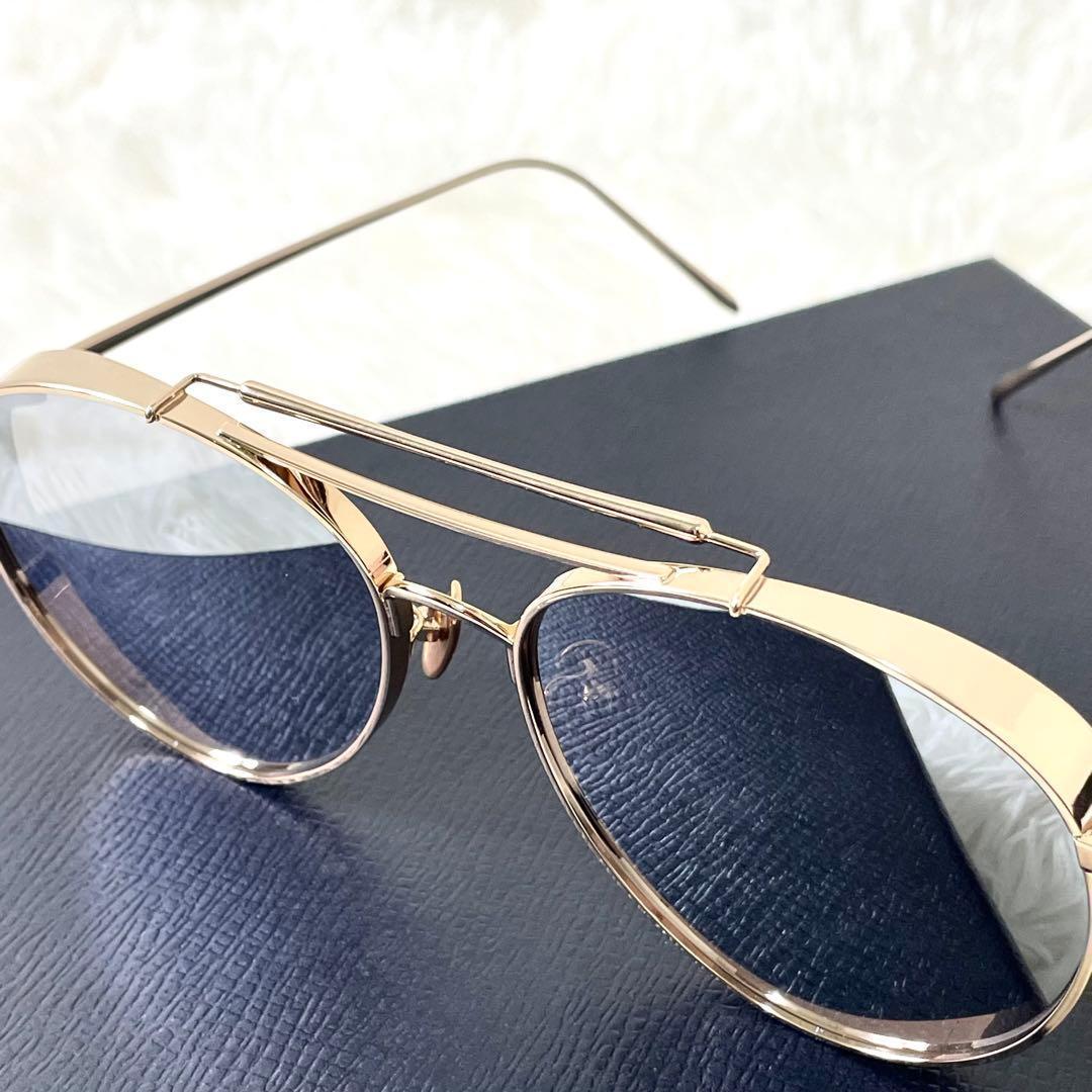 Gold metal sunglasses with dark lenses displayed on a dark textured box.