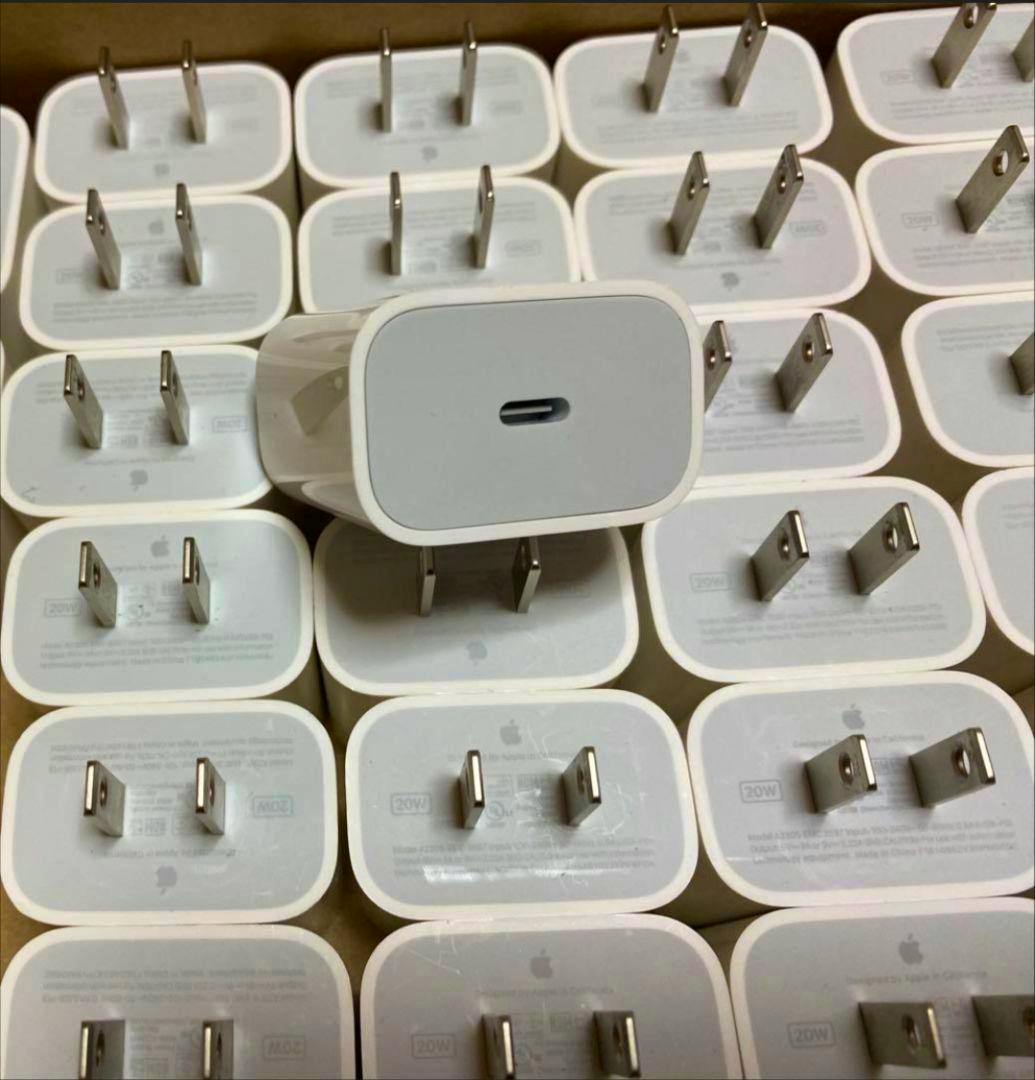 Many white Apple 20W USB-C power adapters arranged in a box with one adapter centered showing the USB-C port.