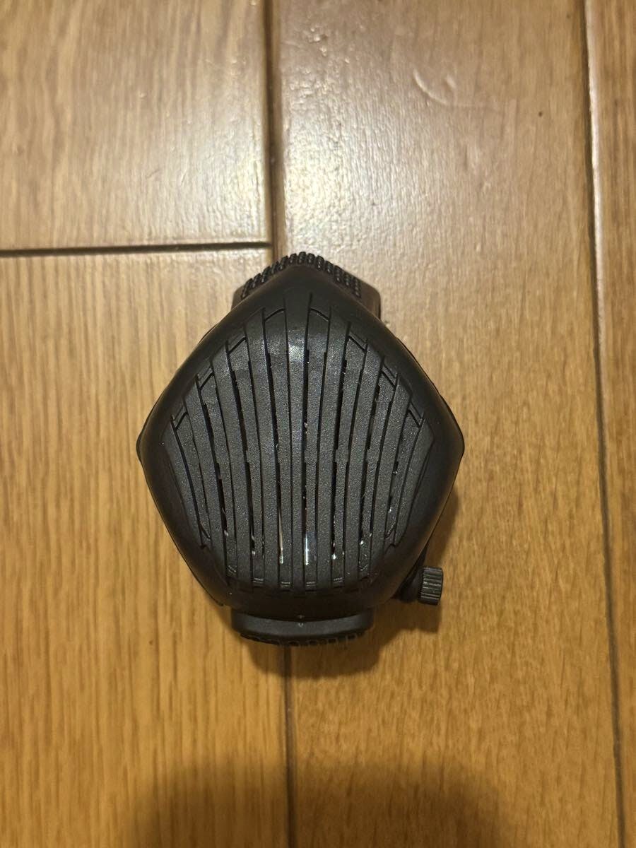 Front view of a black microphone unit for an AVON M50 gas mask placed on a wooden floor.