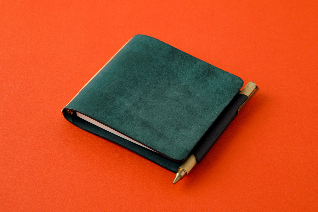 Mini 5 square notebook with a black genuine leather pen holder lifter holding a pen on an orange background.