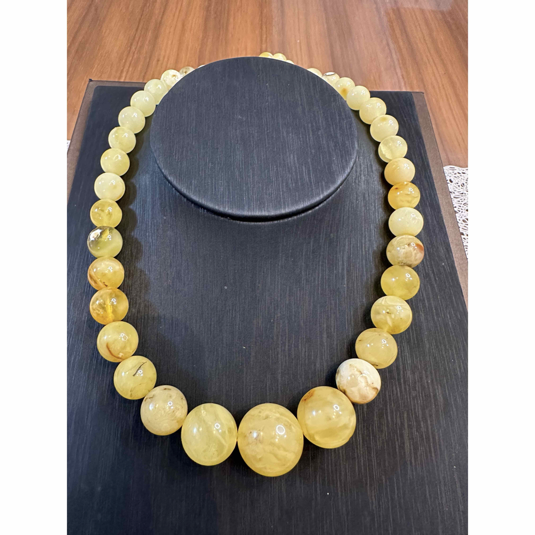 A milky yellow amber bead necklace displayed on a black necklace bust.