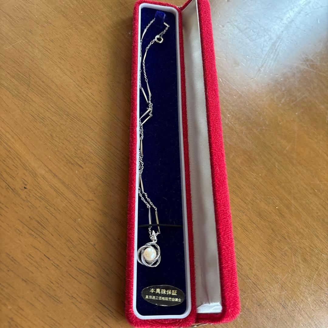 A silver pearl pendant necklace displayed in a red velvet jewelry box on a wooden surface.