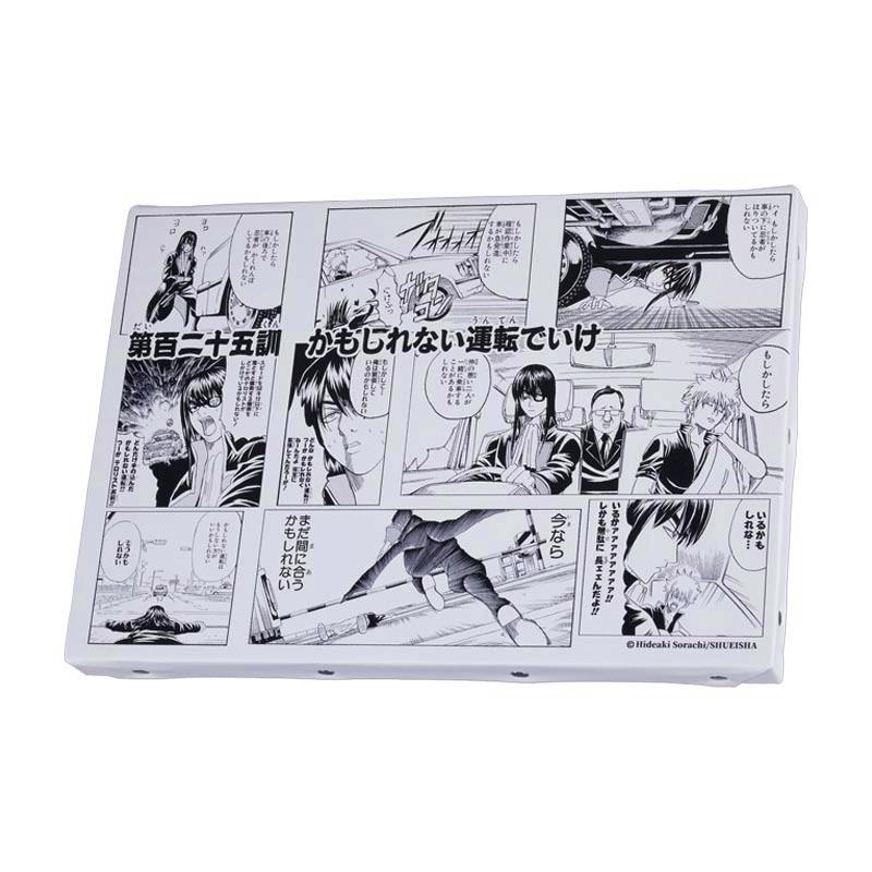 Angled photo of a rectangular art board printed with black-and-white manga panels and Japanese text.