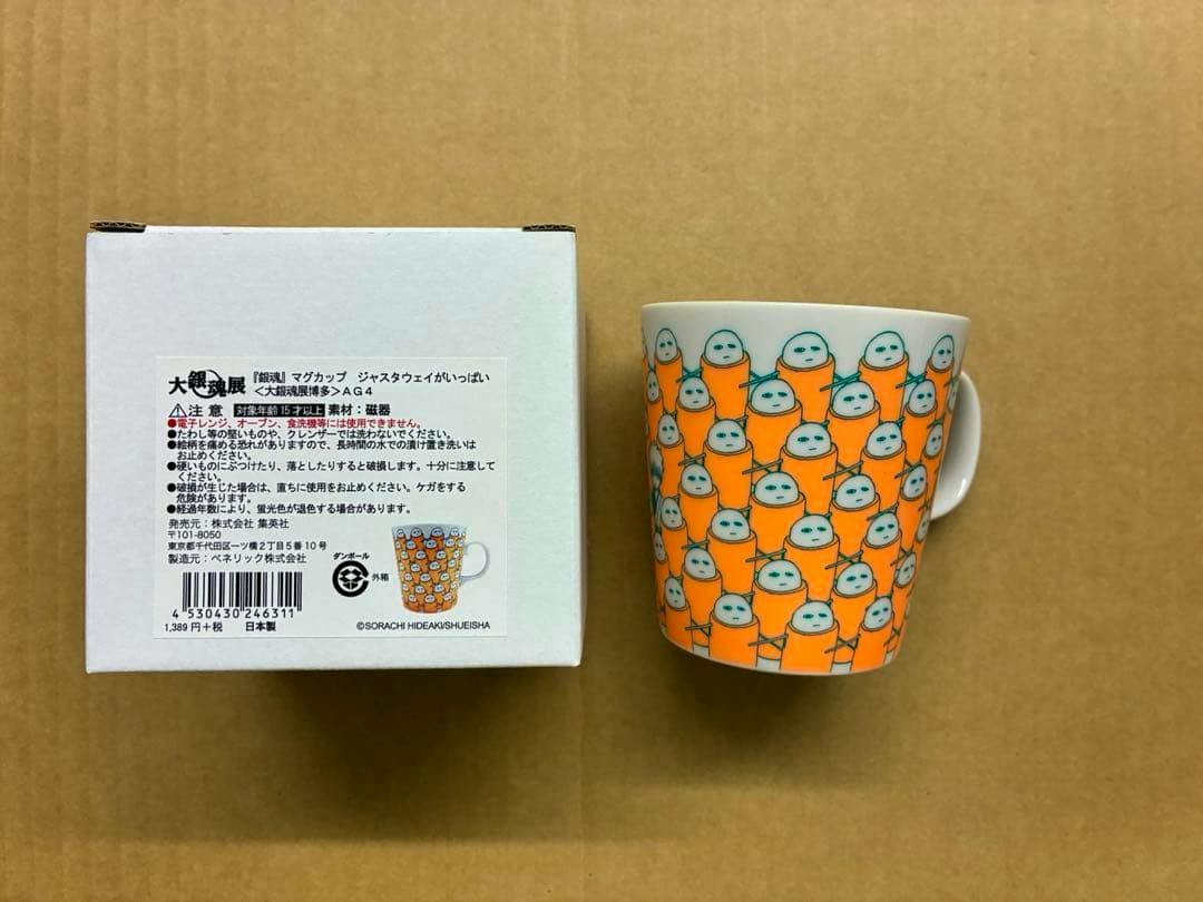 A ceramic mug printed all over with many small orange Justaway characters, pictured next to its white product box.