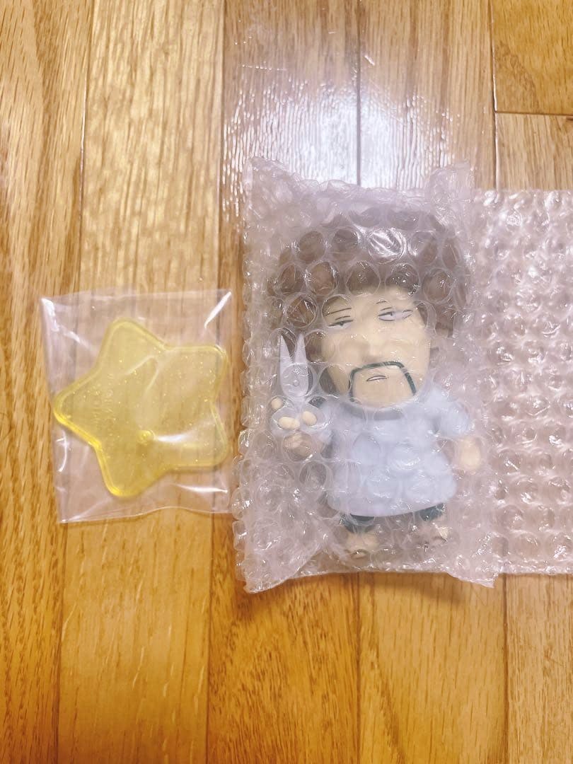 Photo of the plastic figure (wrapped in bubble wrap) alongside a yellow star-shaped base on a wooden floor.