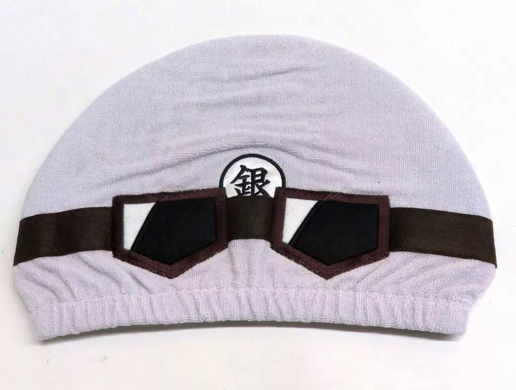 Front view of the towel cap showing a helmet-style design with a brown band, attached goggle shapes, and a circular emblem with the kanji "銀".