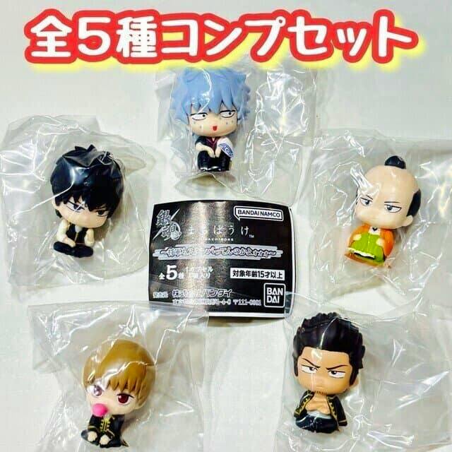 Photo of five individually bagged Gintama machiboke chibi figures arranged around a paper insert.