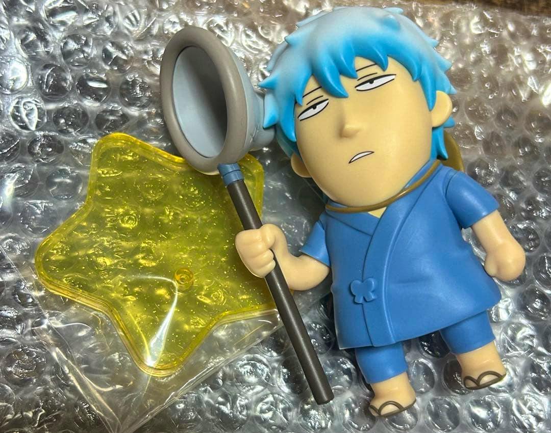 Plastic figure of Sakata Gintoki in blue clothing holding a scoop on a pole, shown with a yellow star-shaped translucent base on bubble wrap.