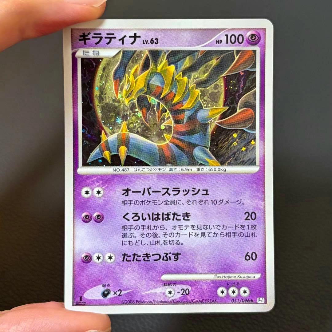 Front of the Giratina LV.63 Japanese trading card (051/096) showing the card artwork and text, held by fingers against a dark background.