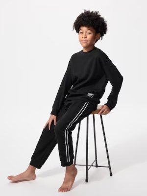 Child model wearing the girls' Airism ultra-stretch long-sleeve set in black while seated on a stool.