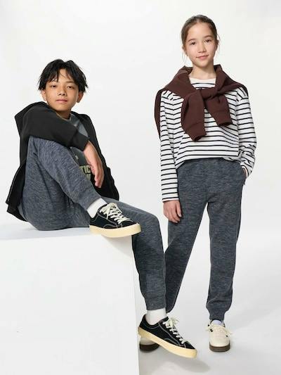 Girl modeling the GIRLS エアリズムウルトラストレッチセット wearing gray stretch pants and a striped top, standing beside a boy.