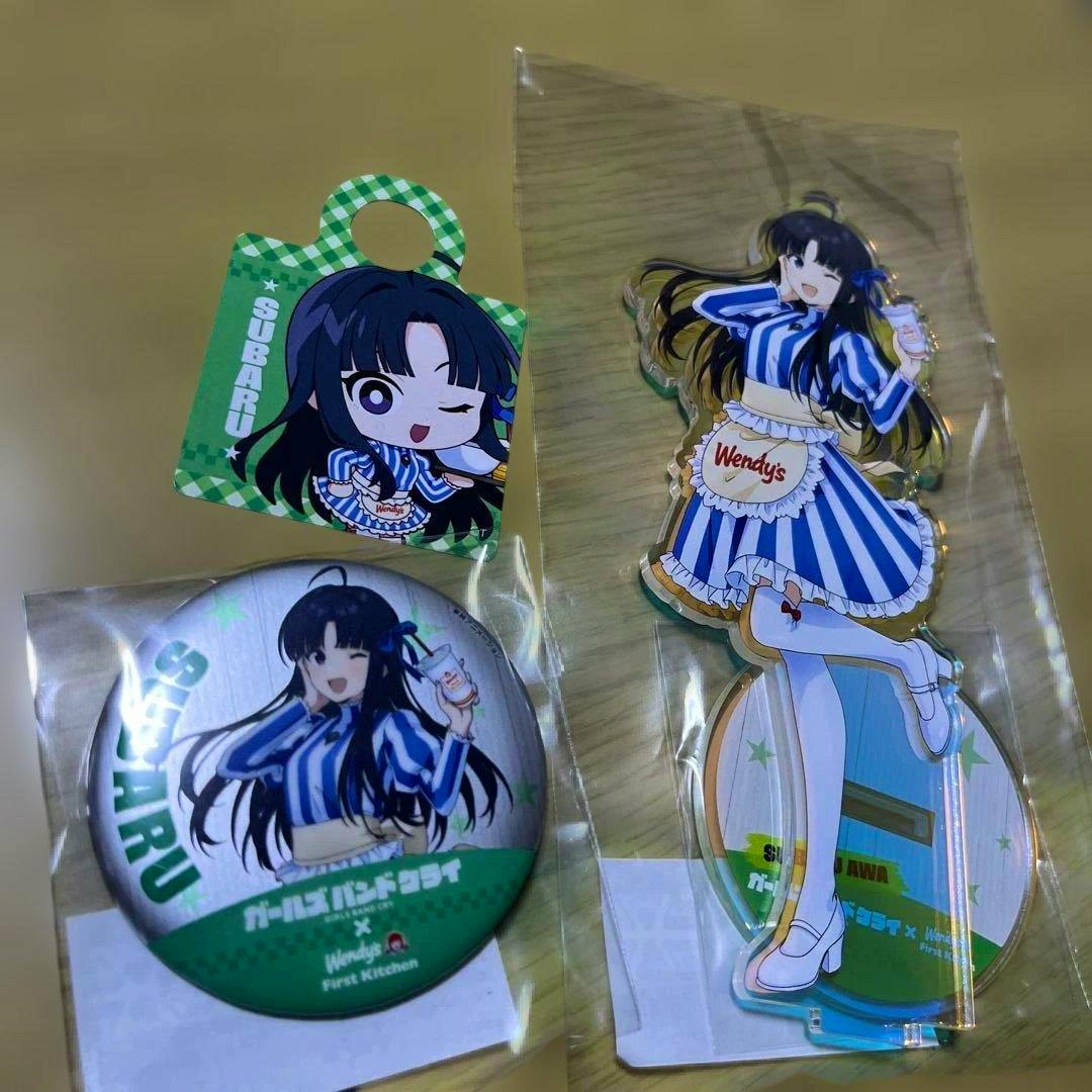 Acrylic stand of Subaru next to a round can badge and character tag showing an anime girl in a blue-striped outfit.