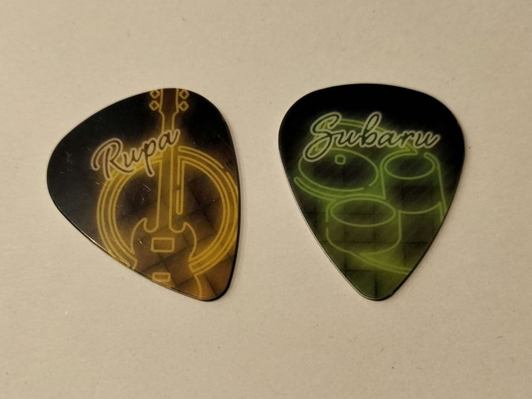Two plastic guitar picks with printed "Rupa" and "Subaru" designs shown on a light background.