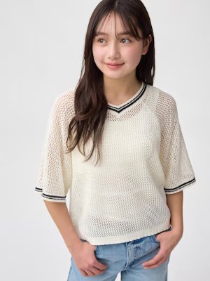 Model wearing a white camisole tank top visible under a white open-knit sweater.