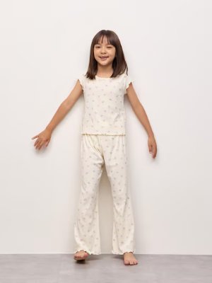 Girl standing against a plain background wearing a short-sleeve lounge set top and matching printed long pants.