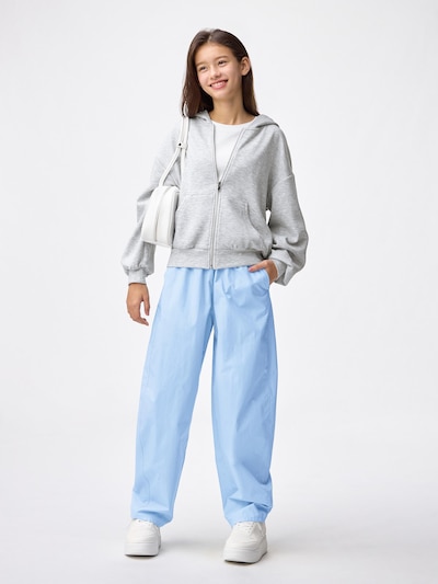Girl wearing light blue barrel-leg pants with a gray zip-up hoodie and white sneakers.
