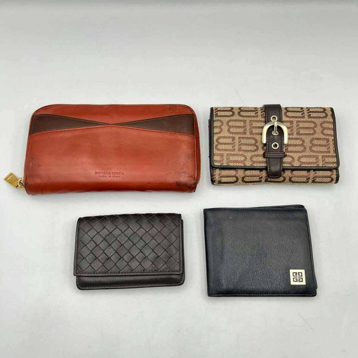 Four wallets and card cases arranged on a white background, including a brown zip BOTTEGA VENETA wallet, a beige monogram buckle wallet, a woven leather card case, and a black Givenchy bifold.