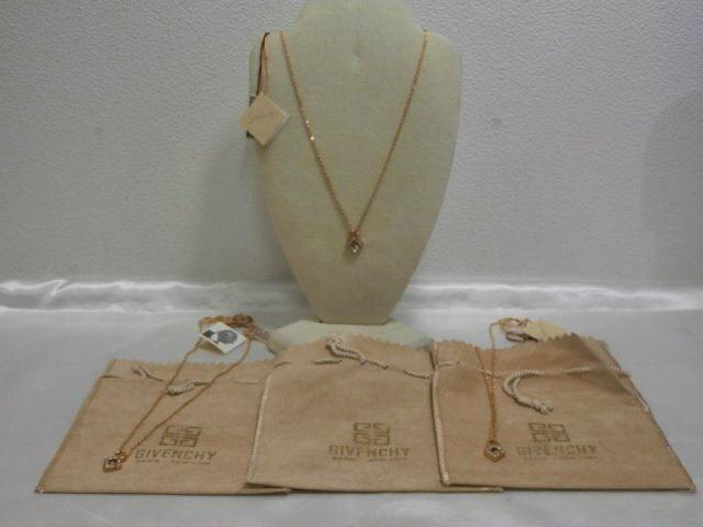 Three gold-colored Givenchy necklaces with G-logo rhinestone pendants displayed on a bust with three Givenchy pouches visible.