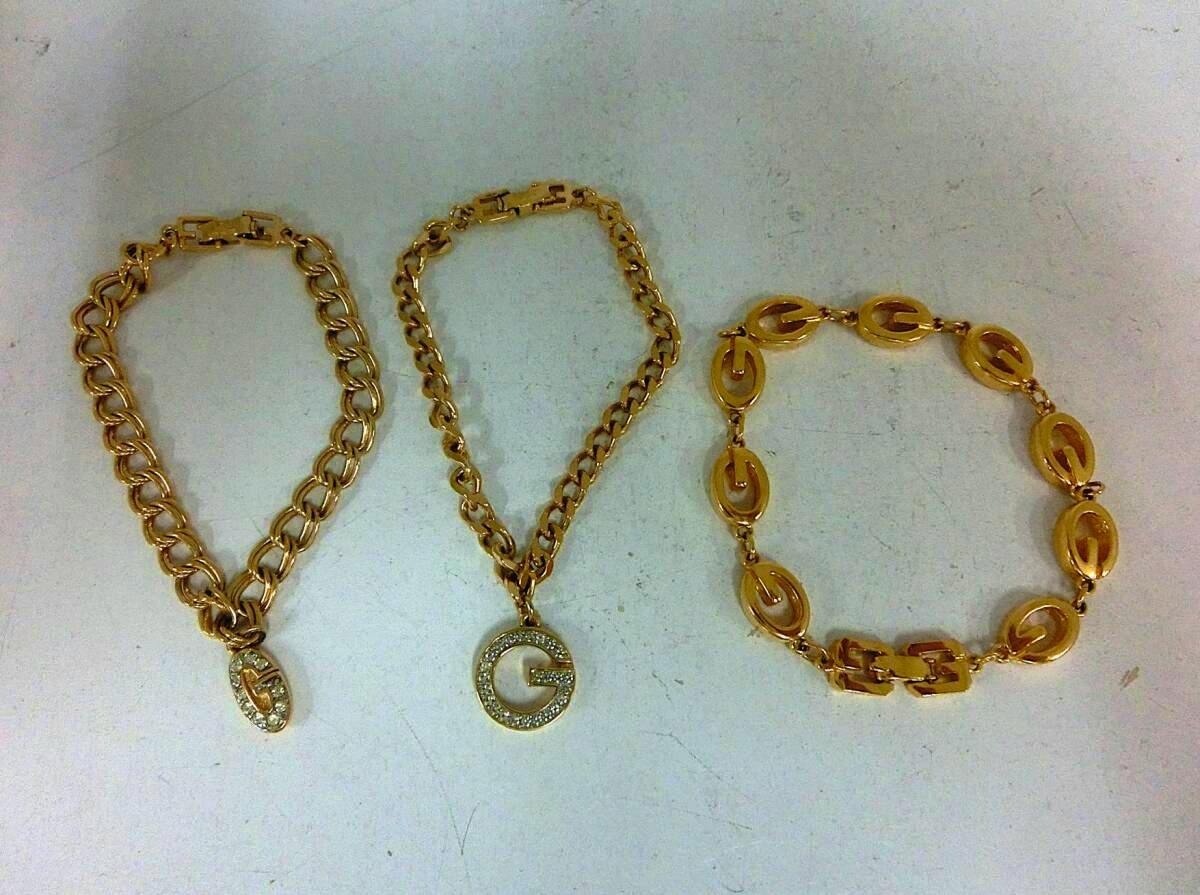 Three gold-colored Givenchy bracelets—two chain styles with G-logo rhinestone pendants and one linked G-logo bracelet—laid on a white surface.