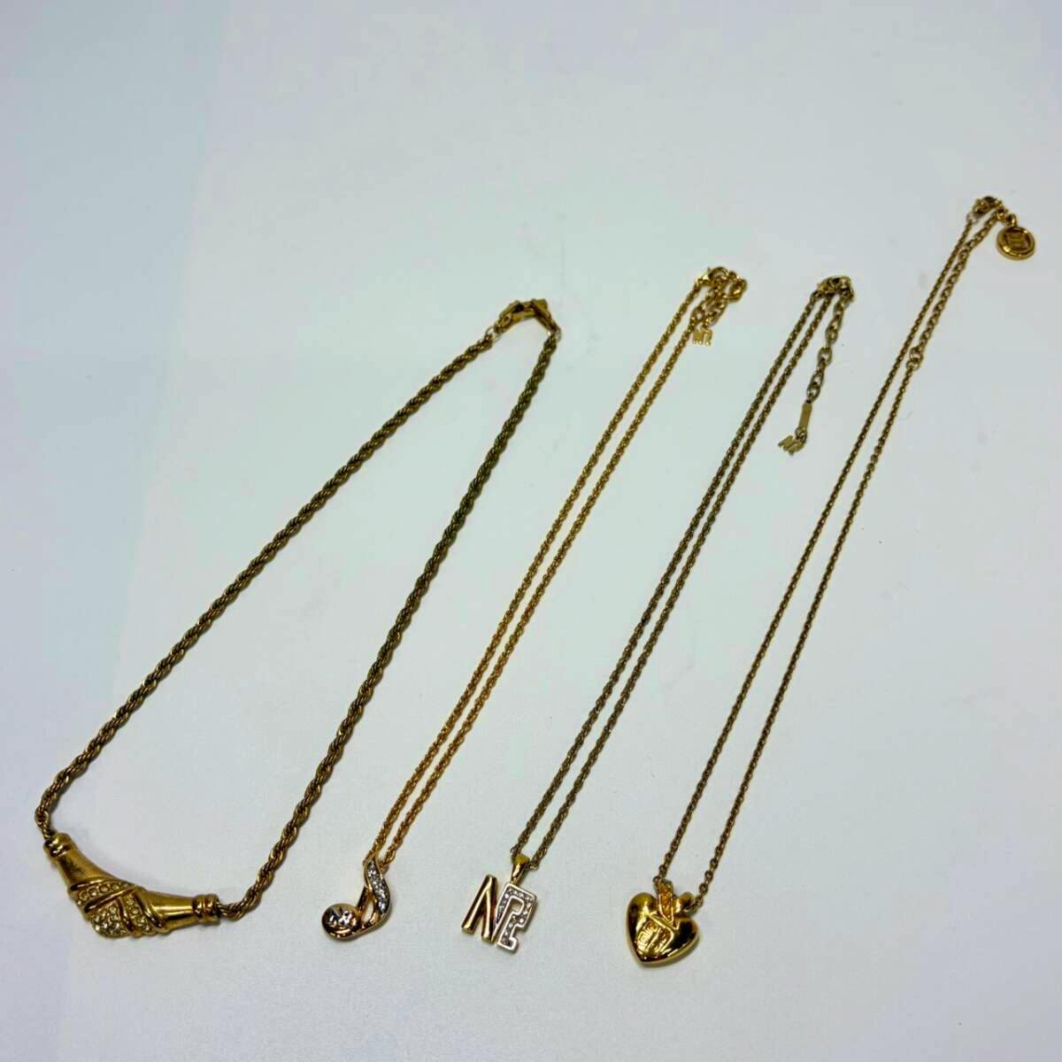 Four gold-colored necklaces with different pendants laid flat on a light background.