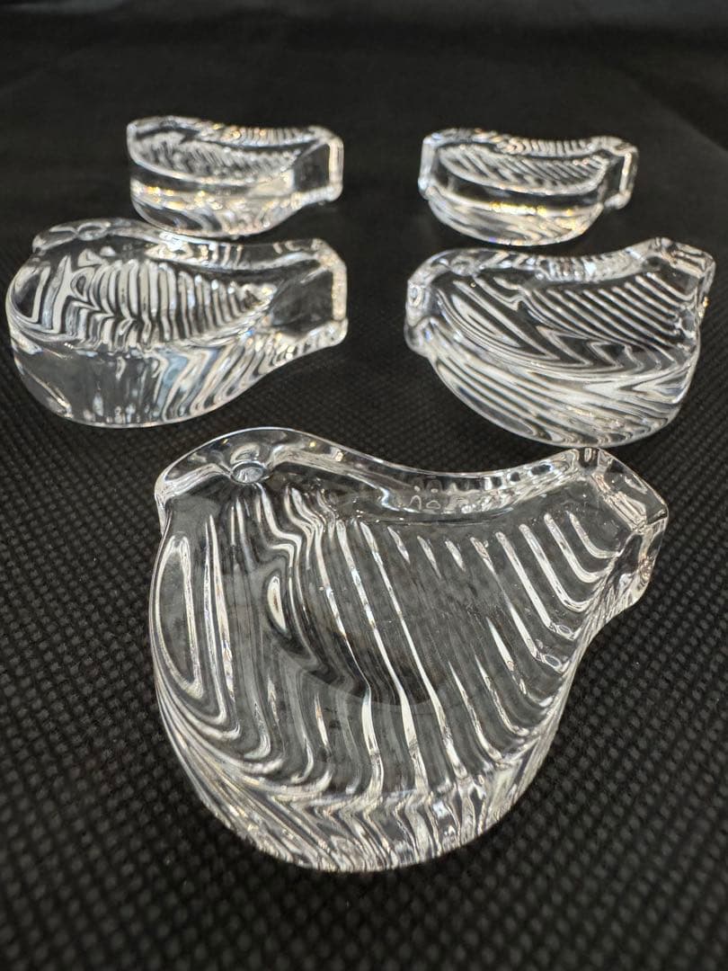 Five clear glass bird-shaped chopstick rests arranged on a black surface in a close-up view.
