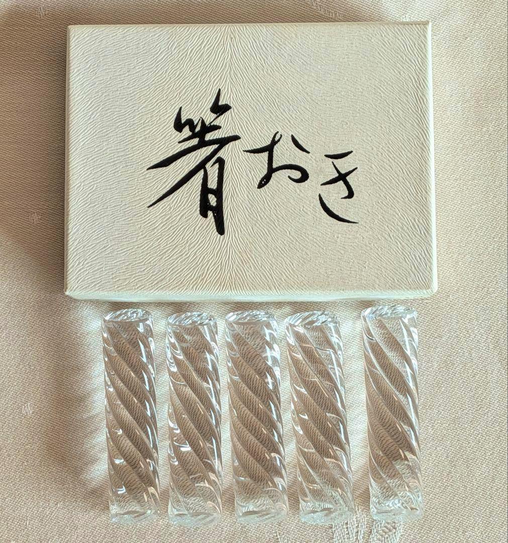 Five clear glass spiral-pattern chopstick rests arranged in a row below a textured box with Japanese writing.