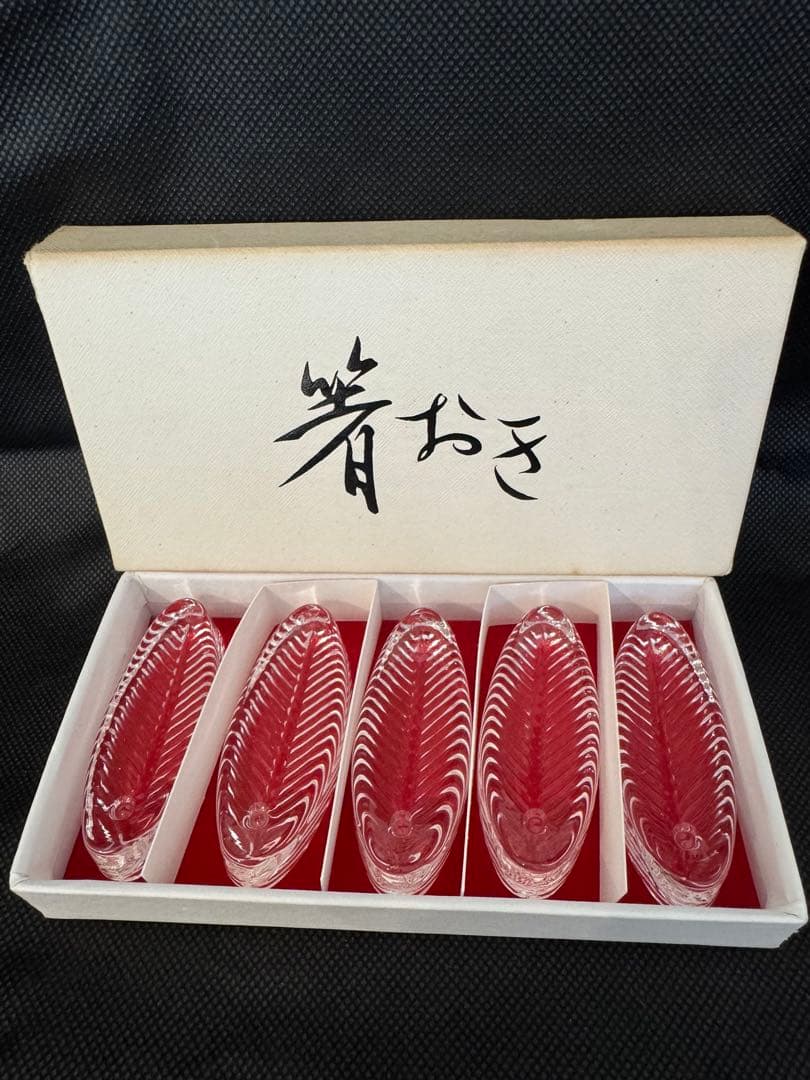 Five glass leaf-shaped chopstick rests displayed in a white box with a red interior.