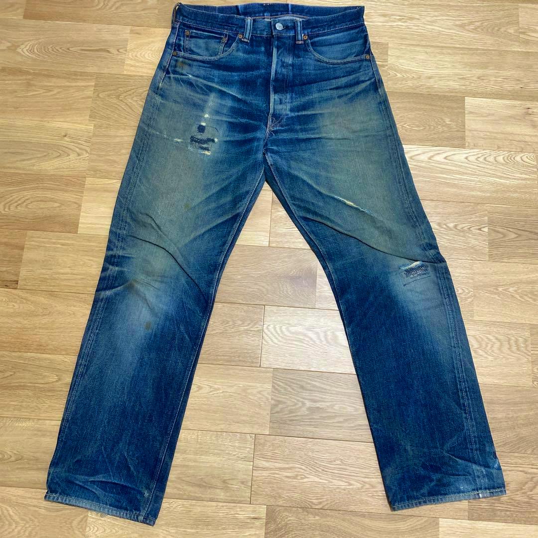 Front view of the GLEEM 200XX men's jeans (W31) laid flat on a wood floor showing fading and repaired distressing.