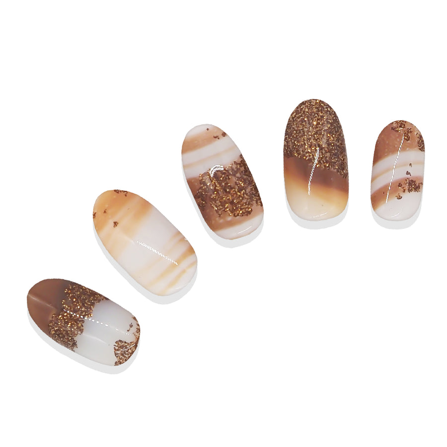 Five brown, white, and glitter nail stickers shown on display nail tips against a white background.