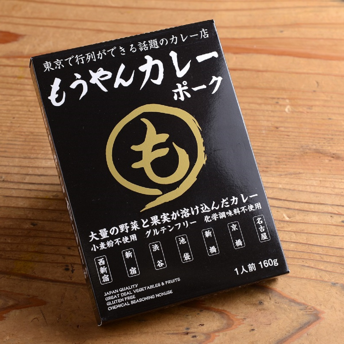 A single black boxed package of the pre-packaged pork curry with Japanese text and a gold logo sitting on a wooden surface.