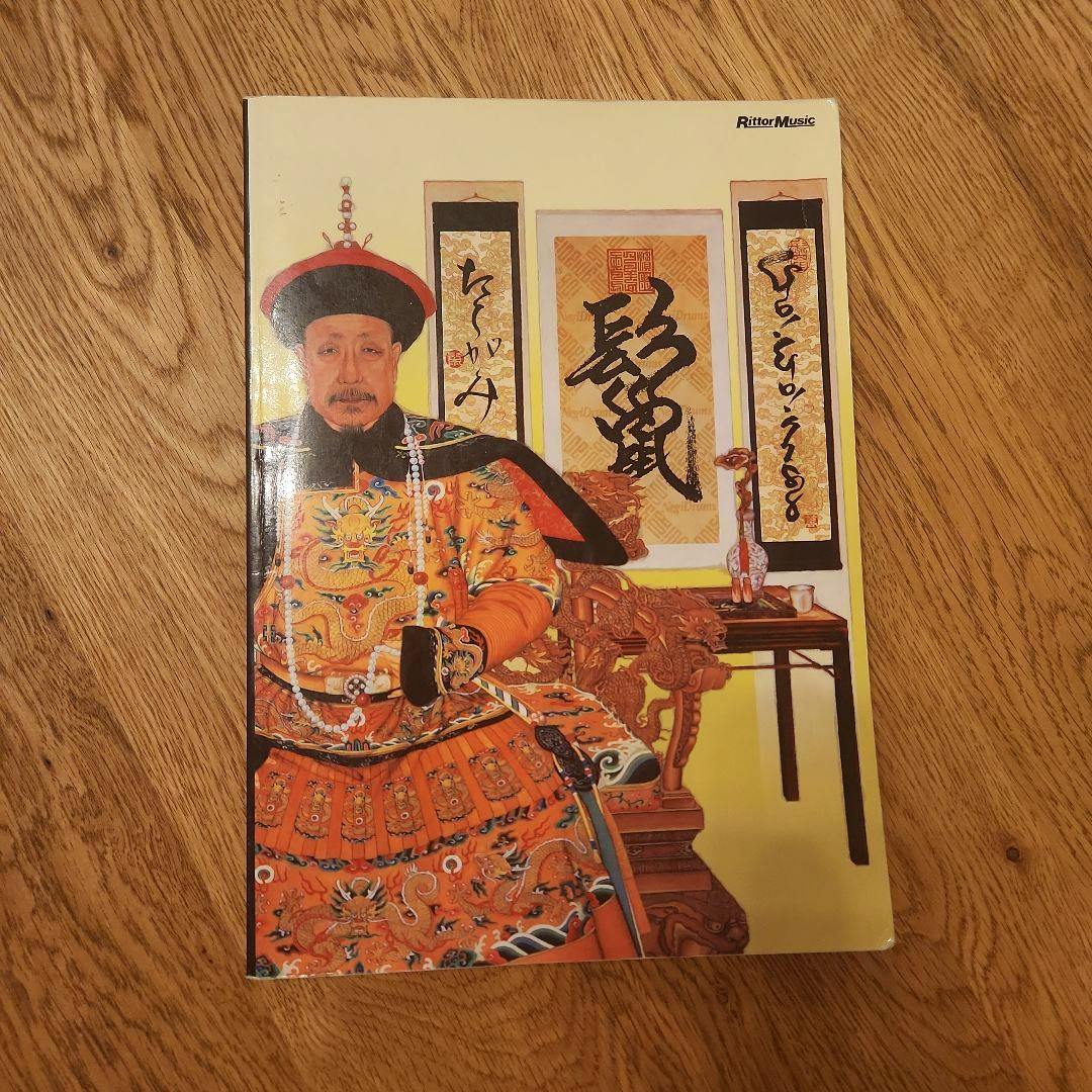 Photograph of the front cover of the GO!GO!7188 band score book showing an illustrated seated man in ornate traditional robes.