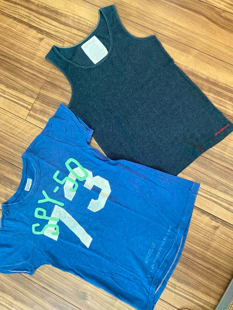 Two cotton T-shirts for 150cm laid flat on a wooden floor: a blue short-sleeve printed T-shirt and a dark gray sleeveless tank.