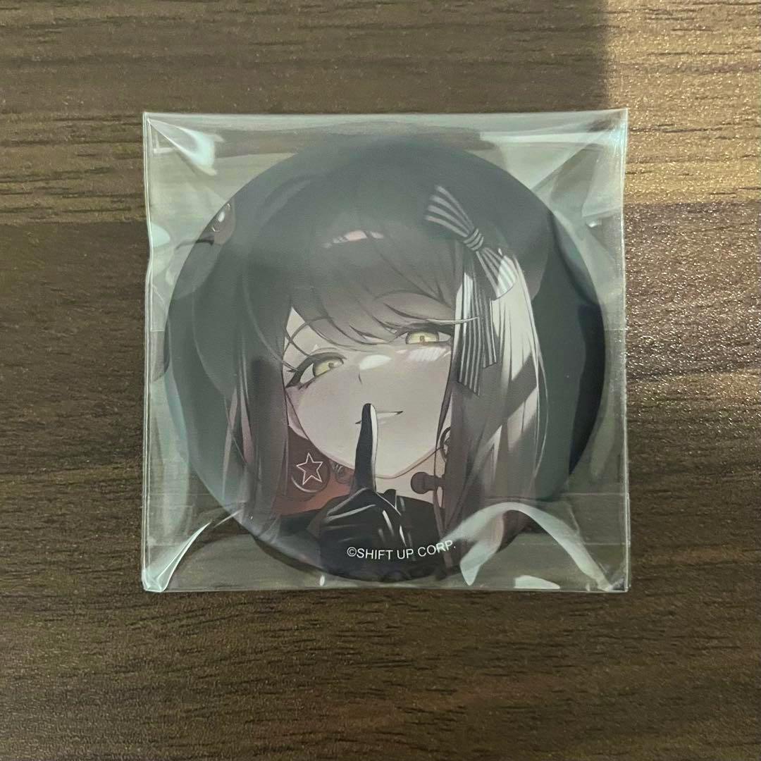 Photo of a round NIKKE バースト缶バッジ Vol.5 featuring Emma in sealed plastic packaging on a wooden surface.