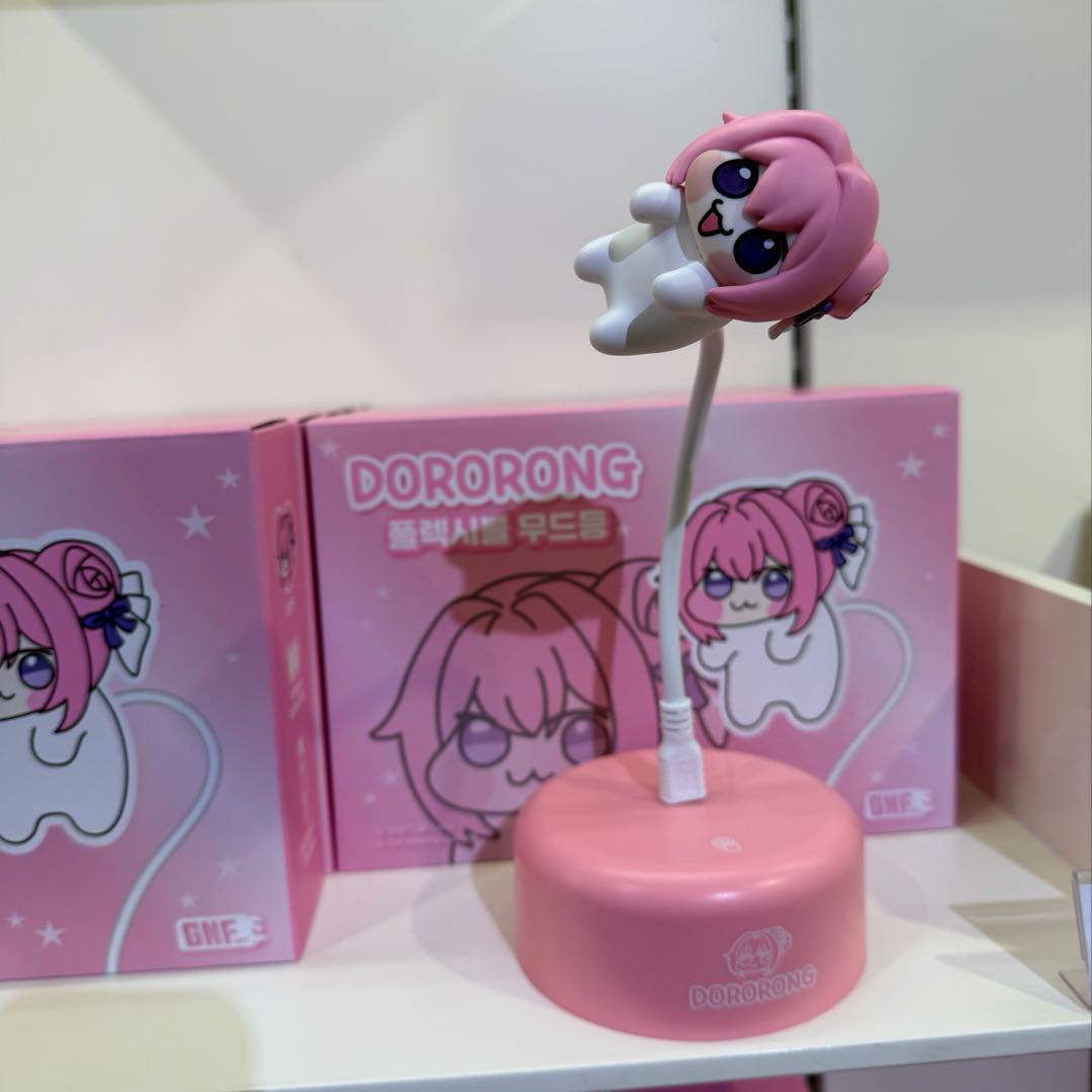 Pink DORORONG desk LED lamp with a pink character figure on a flexible neck shown on a shelf next to its boxes.