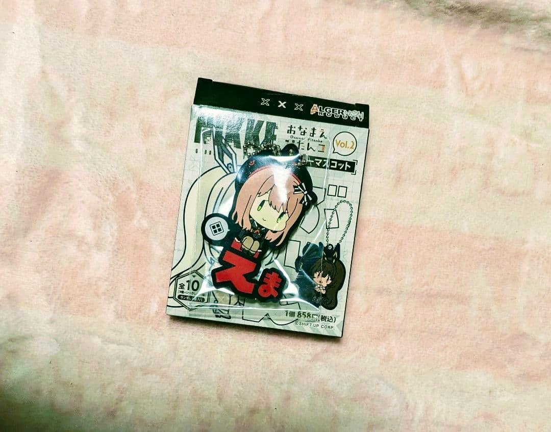 Packaged 勝利の女神 NIKKE おなまえぴたんコ vol.2 rubber strap featuring Emma placed on a pink surface.