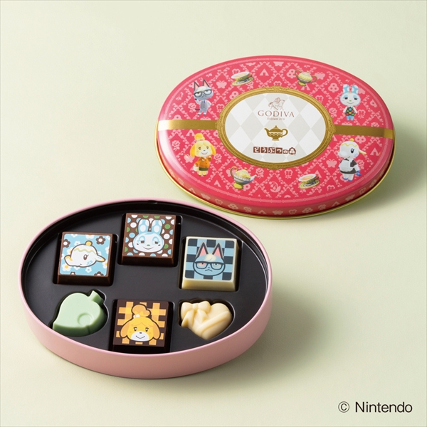 Open pink oval Godiva tin marked for どうぶつの森 showing six assorted Animal Crossing–themed chocolates with the matching lid beside it.
