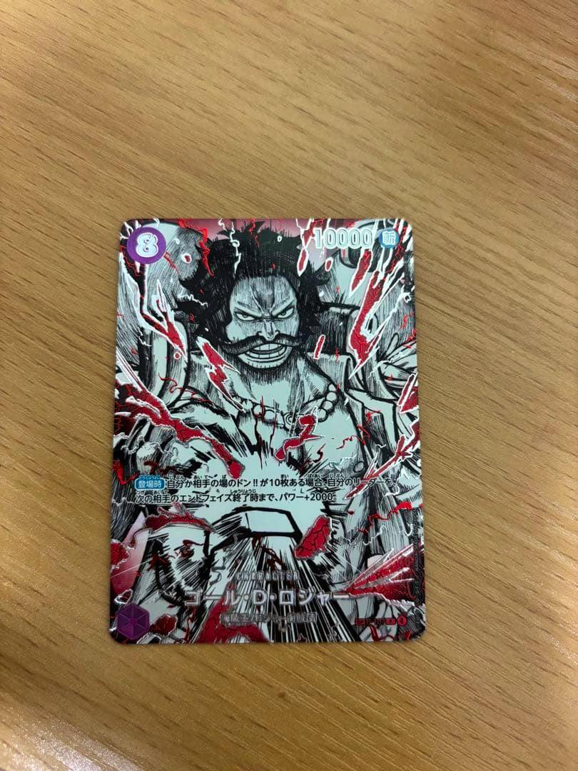 Front of the trading card ゴール・D・ロジャー (覇王色SP) P-107 showing the card's illustrated face on a wooden surface.
