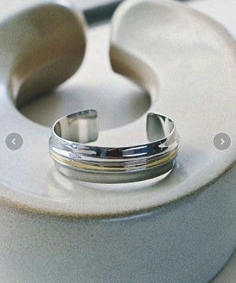 Close-up of the gold combination bold metal bangle showing silver body with a gold stripe, displayed on a round neutral stand.