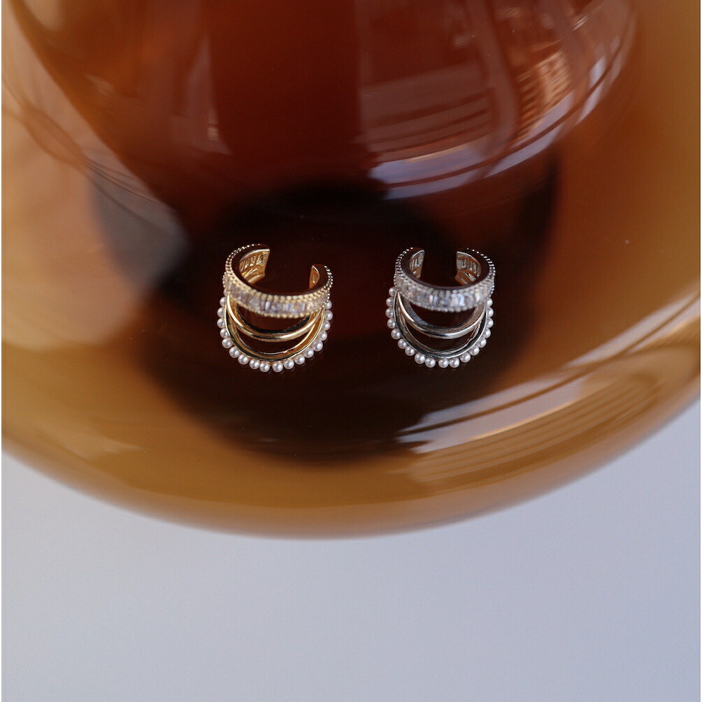Two gold-tone three-row ear cuffs with pearl beads and zirconia stones placed on a brown dish.