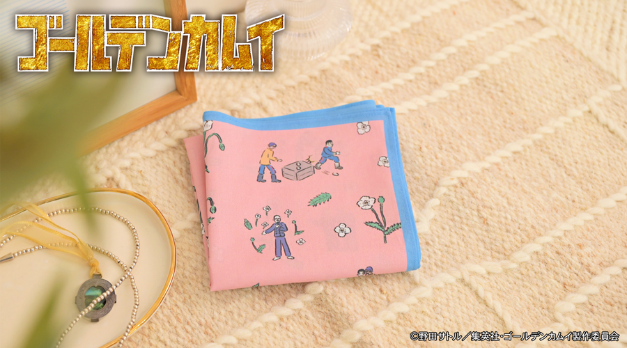 Folded pink cotton bandana with a blue border and small illustrated characters resting on a textured surface.
