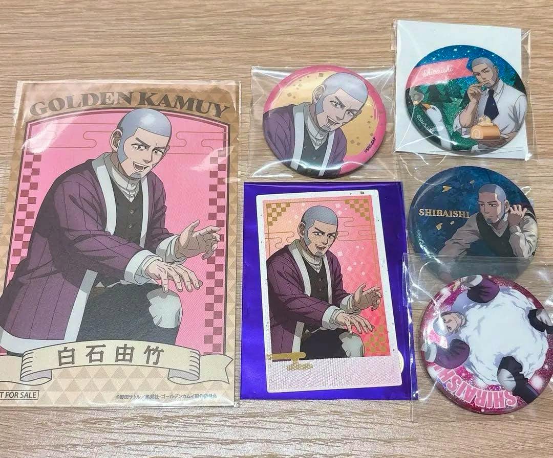 Several Golden Kamuy Shiraishi can badges and related paper goods arranged on a wooden surface.